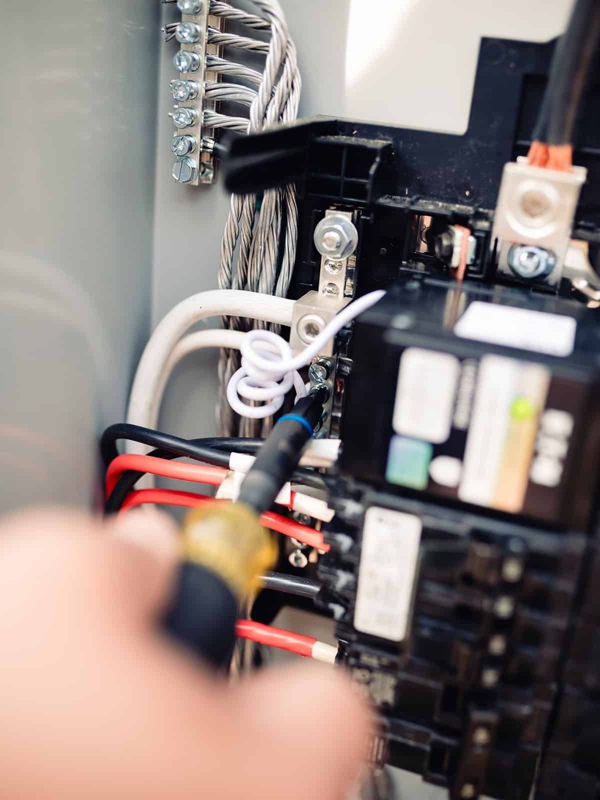 Close-up of an electrician using a screwdriver to tighten wire connections inside a residential electrical panel
