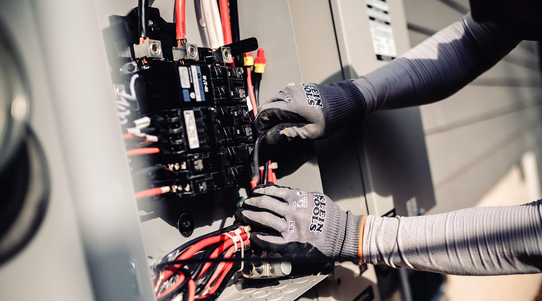 Close-up of an electrician's gloved hands routing wires inside an open outdoor electrical panel
