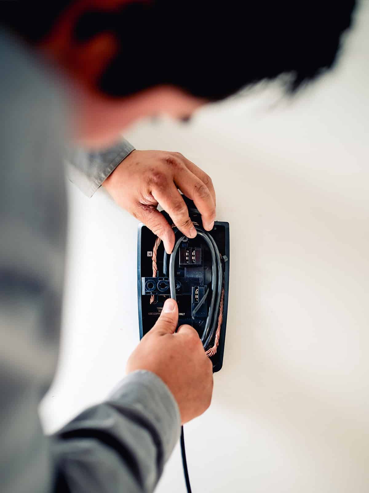 Overhead view of an electrician wiring the back of an EV charger unit being mounted to a wall
