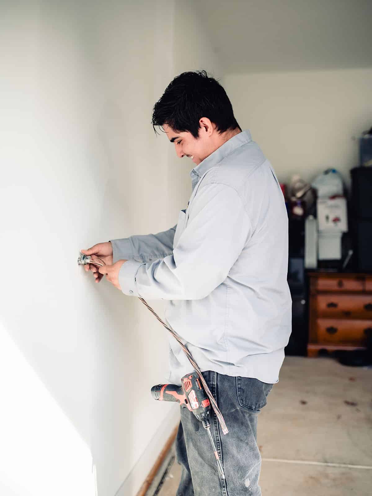 Electrician feeding copper wire into a wall during an electrical installation in a residential garage