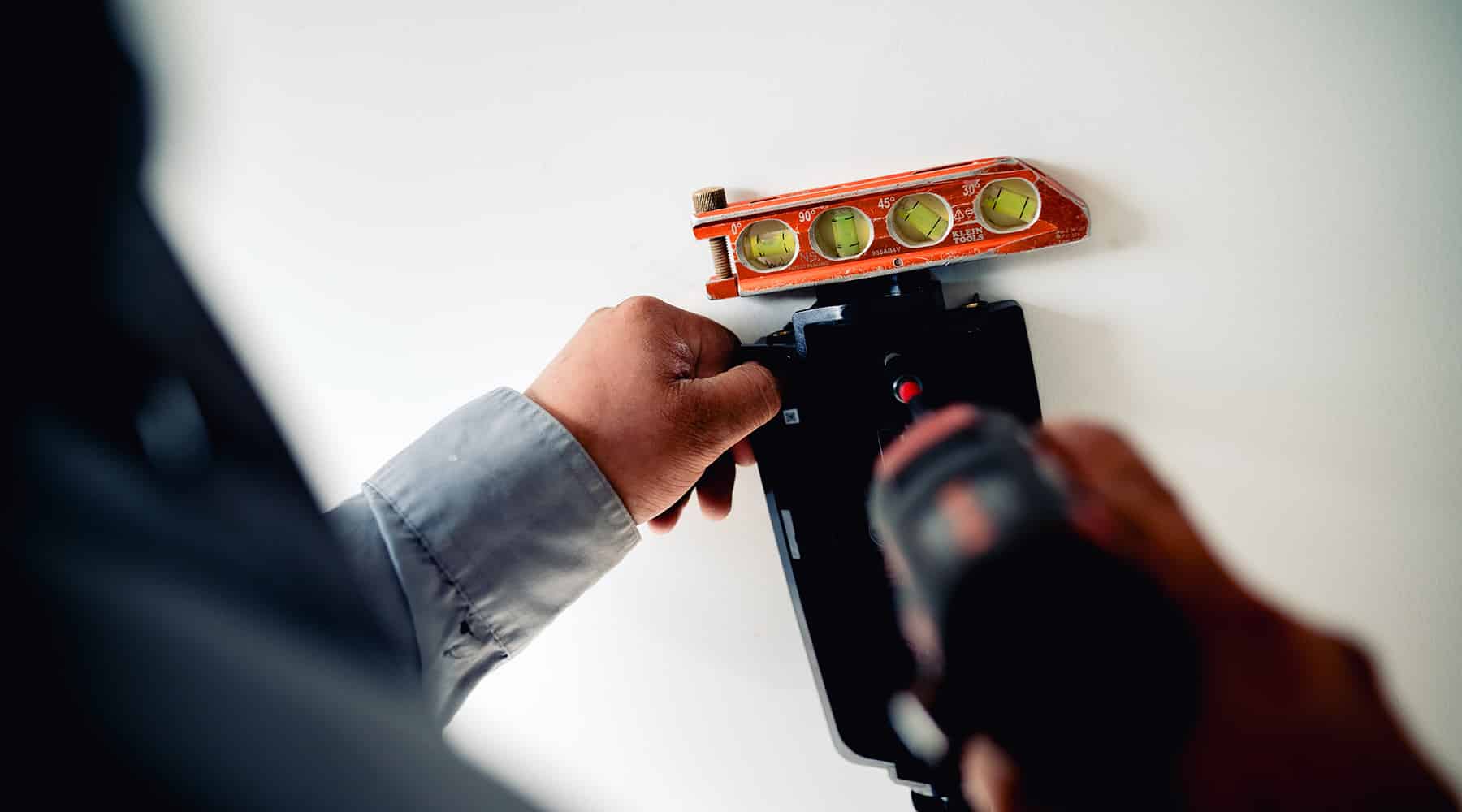 Electrician using a bubble level and drill to mount an EV charger flush on a wall