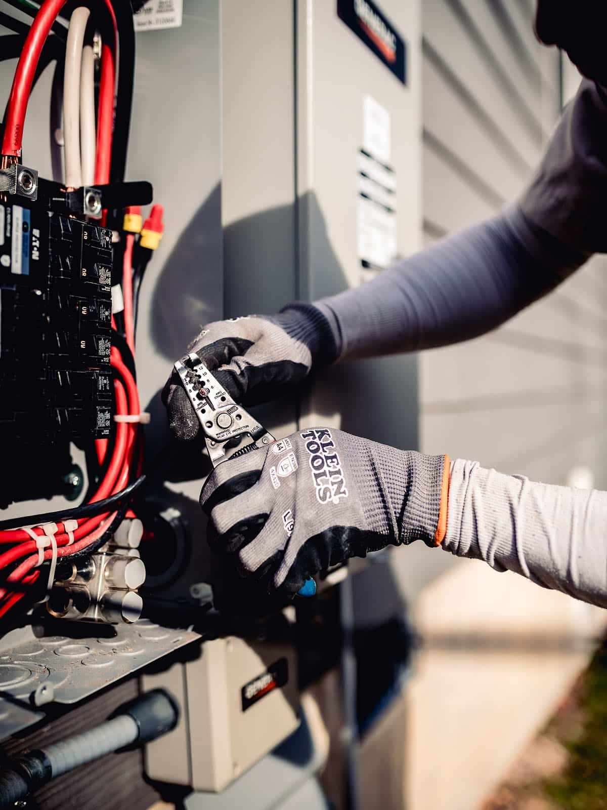 Gloved electrician's hands using a wire stripper tool on wiring inside an outdoor electrical panel