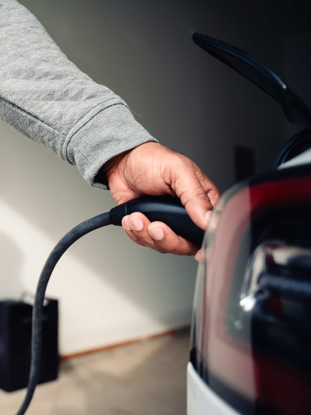 Close-up of a person plugging an EV charging cable into an electric vehicle in a garage