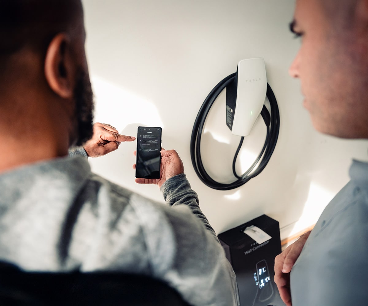 Bee Bright Electrical technician showing a homeowner the Tesla app on a smartphone next to a newly installed Tesla Wall Connector in Cary, NC.